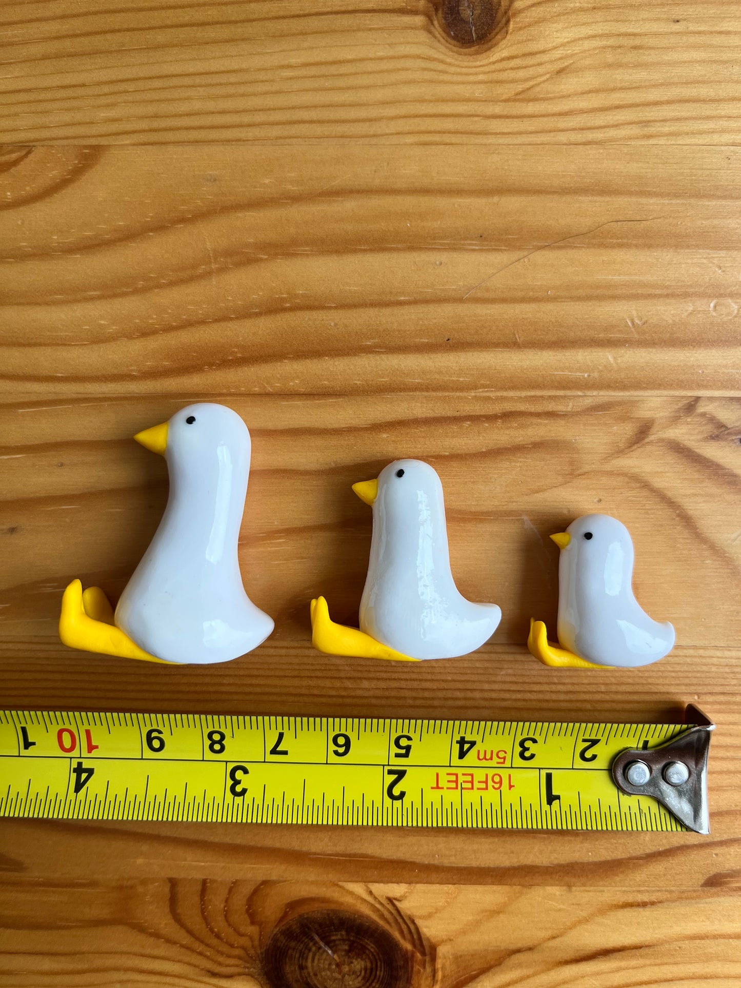 Three small white and yellow bird figurines next to a ruler on a wooden surface