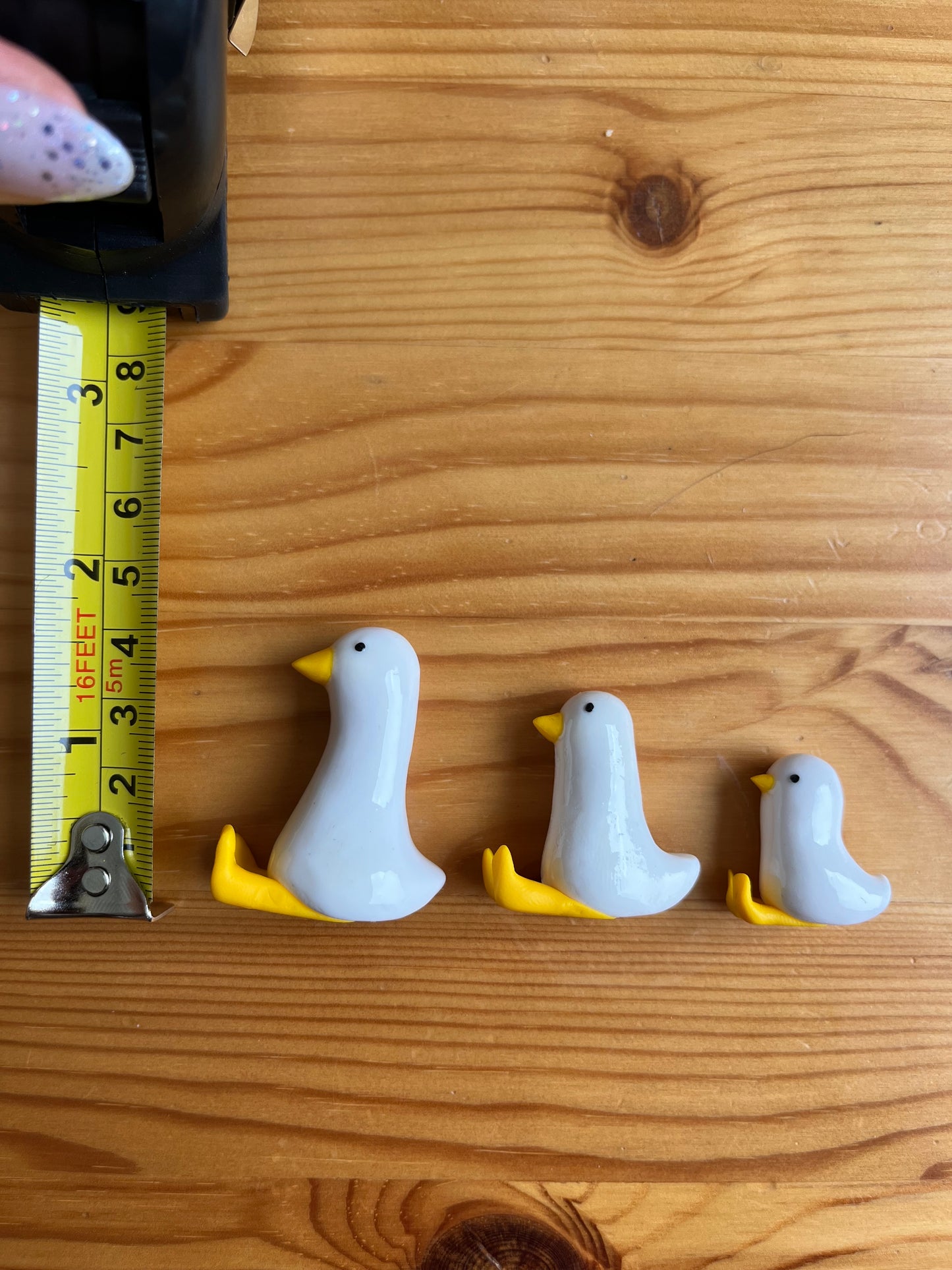 Three small duck-shaped objects on a wooden surface with a measuring tape for scale.